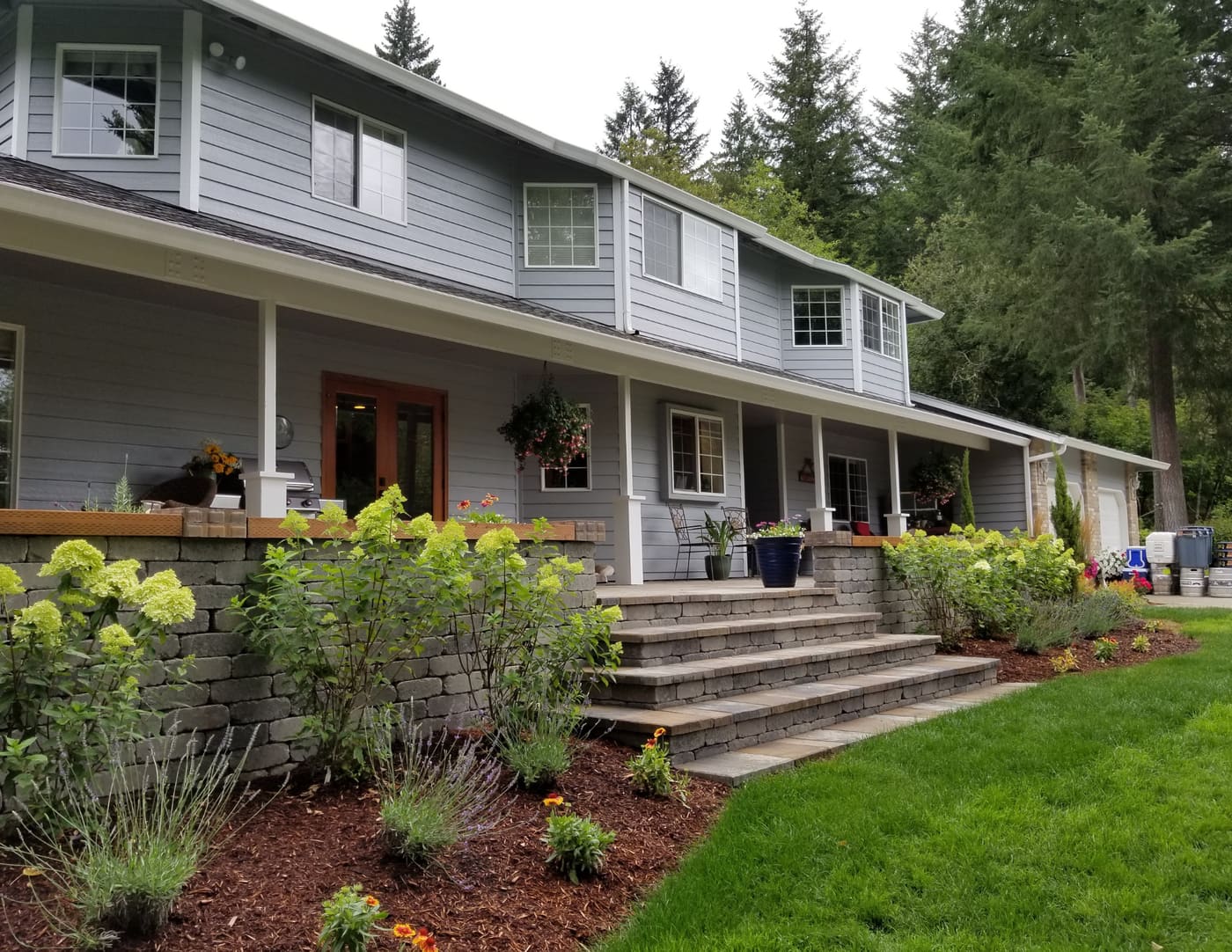 Wide block-and-paver steps leading to a covered porch, flanked by block walls, pale green hydrangeas, and mulched flower beds in Brush Prairie