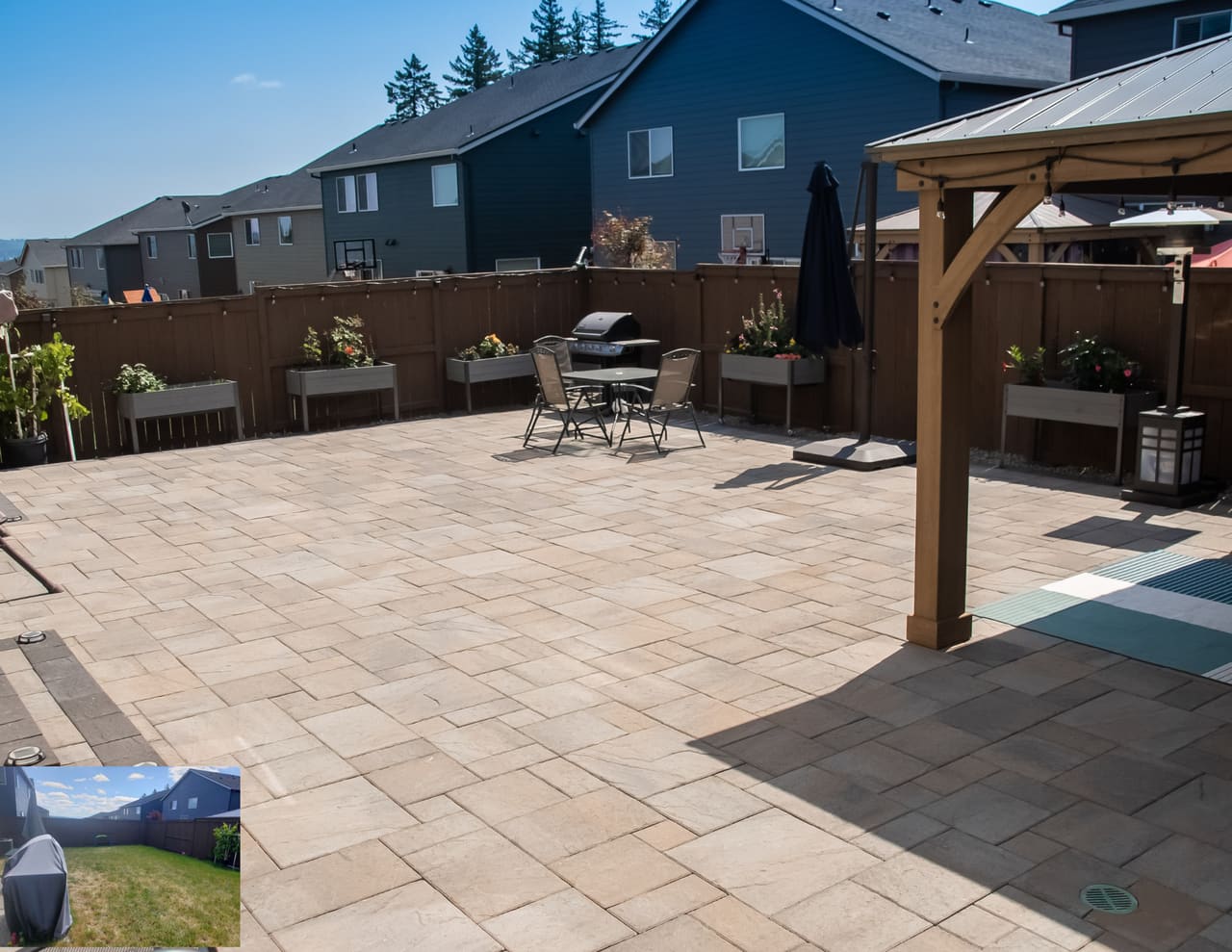 A backyard paver patio with raised planter beds and a wood patio cover for shade.
