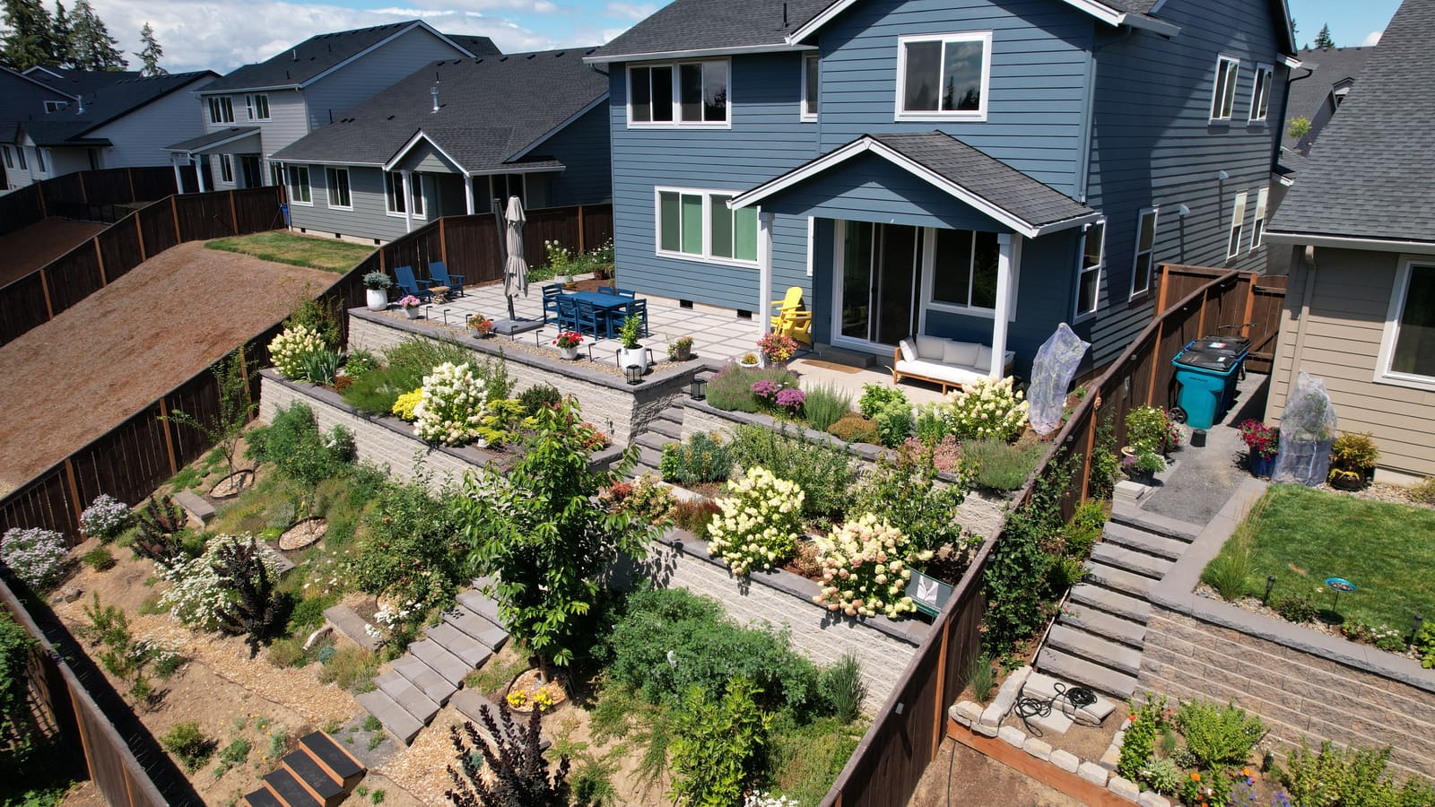 Aerial view of terraced block retaining walls with flowering planting beds, connecting stone stairs, and an upper patio.