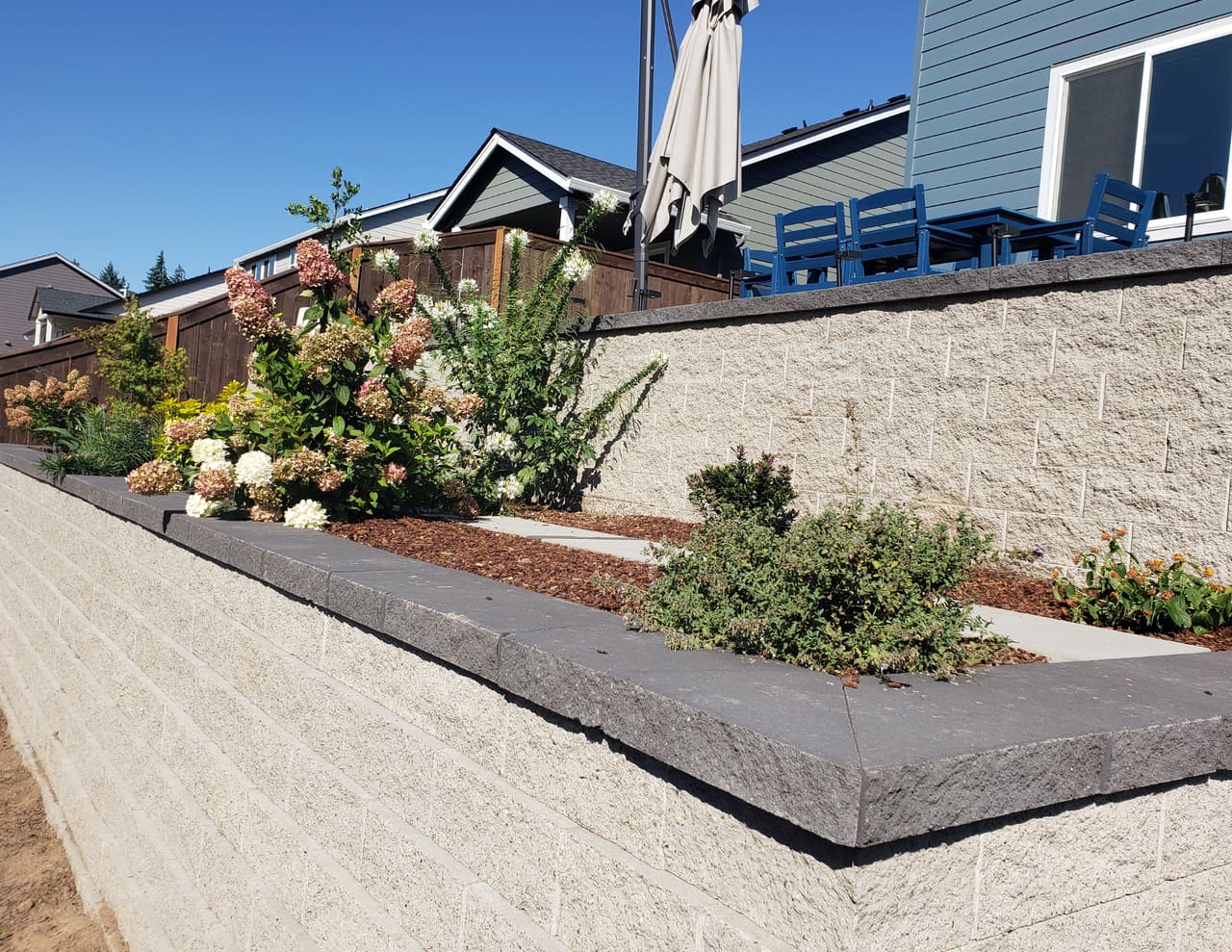 A modular block retaining wall with terraced plantings and a paver sitting area.